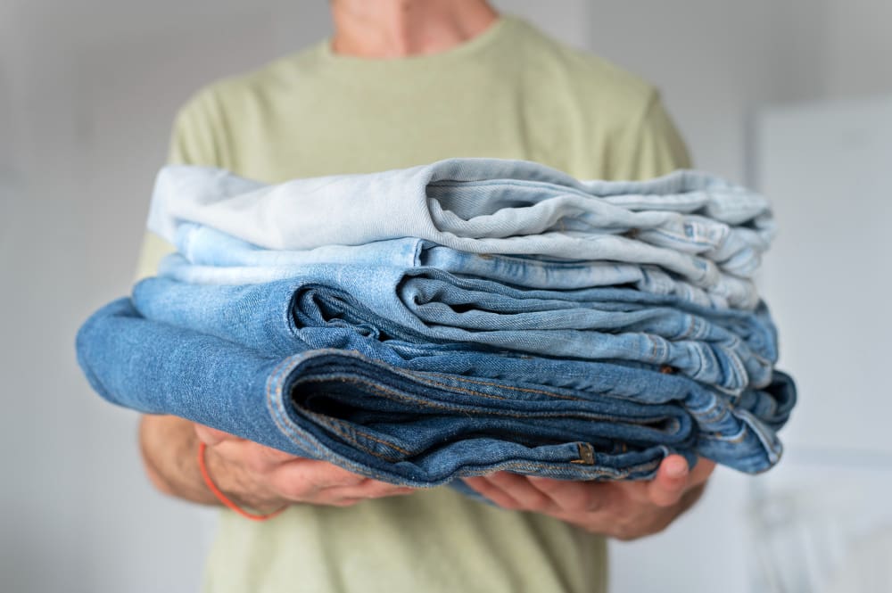 A person holding a stack of folded blue and light-wash jeans, wearing a light green t-shirt.