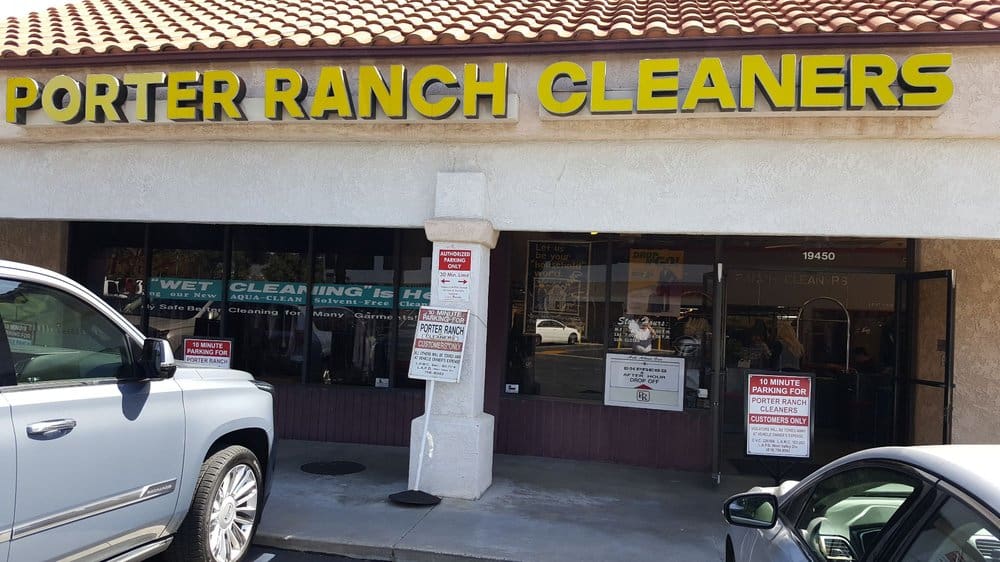 Storefront of Porter Ranch Cleaners with yellow signage, a parked SUV in front, and signs indicating 10-minute parking for customers only.