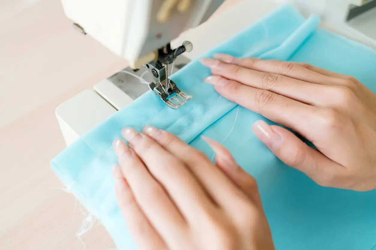 Close-up of hands guiding blue fabric through a sewing machine, stitching a seam.