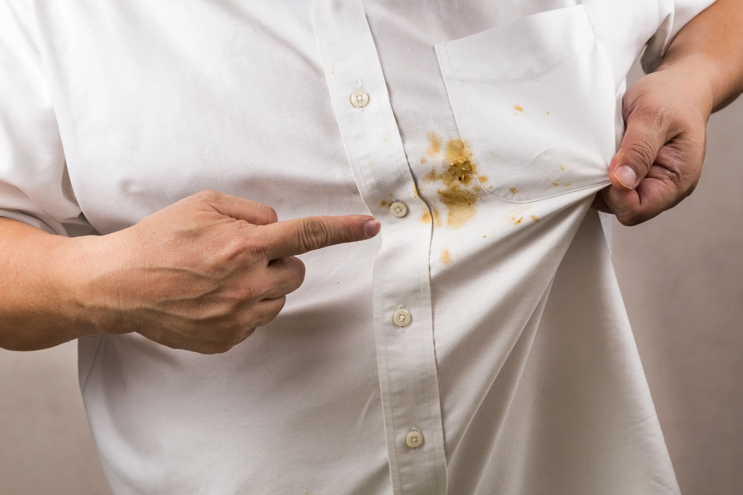 A person points to a noticeable brown stain on the front of their white button-up shirt.